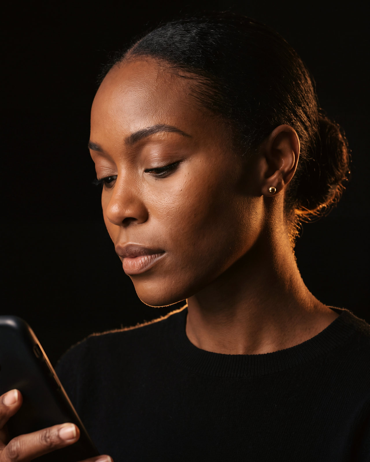 A woman reads her phone in a dark room, her face lit by its warm glow