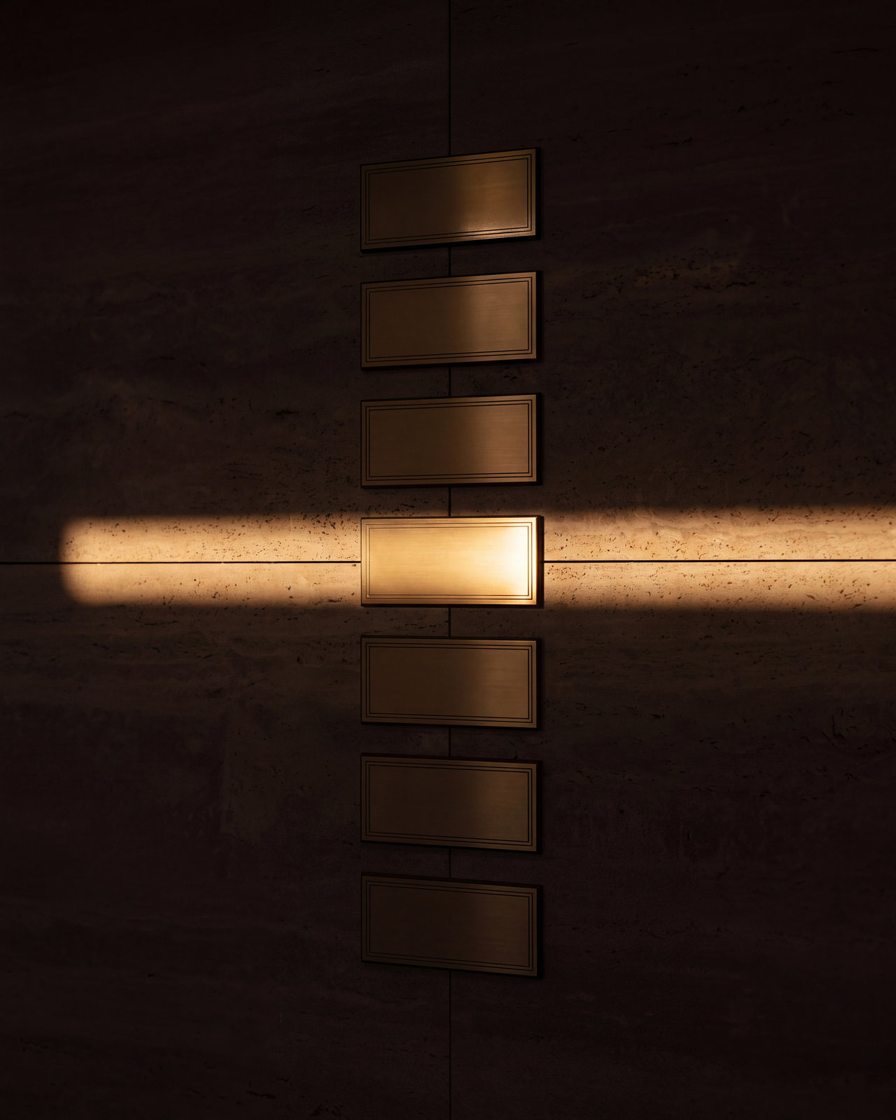 A column of brass name plaques on travertine, one caught in a single blade of light